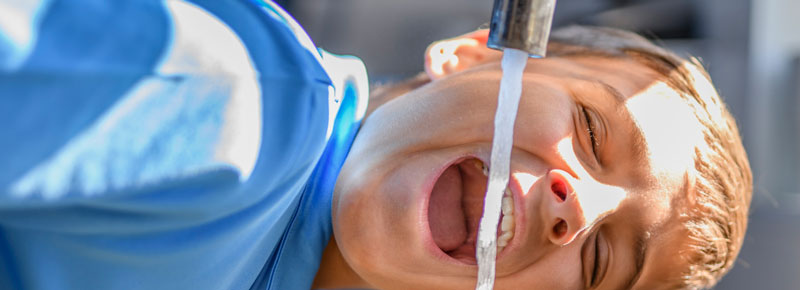 Boy leaning over kitchen sink drinking filtered water out of the tap.