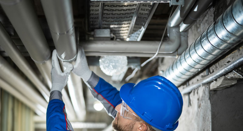 Plumber looking at industrial plumbing on basement ceiling.